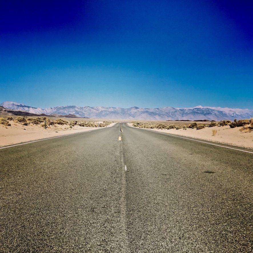 An empty two-lane highway running toward distant mountains under a deep blue sky